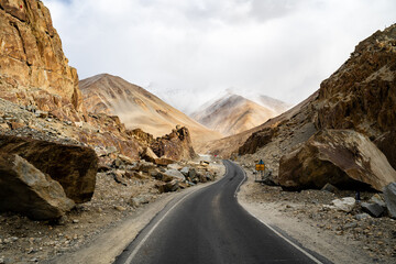 Spectacular high roads wind through rugged mountains beneath blue skies and the remote snow-capped peaks of Ladakh, India.