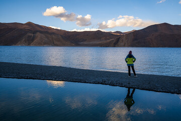 A person standing with arms raised at a serene mountain lake during sunset, reflecting the joy of nature.