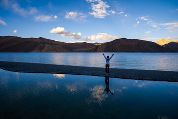 A person standing with arms raised at a serene mountain lake during sunset, reflecting the joy of nature.