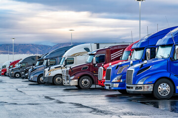 Pro industrial big rigs semi-trucks with semi trailers standing in row on the wet truck stop...