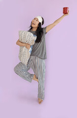 Full body smiling happy young Asian woman wears pyjamas jam sleep eye mask rest relax at home hold pillow look camera isolated on plain pastel pink background. Good mood night nap concept