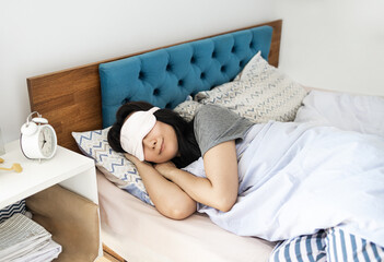 Top view Asian young woman wear pajama and eye mask lying in bed sleep spend time in bedroom lounge home in own room hotel wake up dream. Real estate concept. 