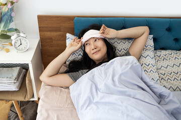 Top view of young Asian woman waking up in early morning lying on bed with linen and stretch her arms and body with smile
