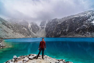 young man standing in front of of laguna 69 with in snow-covered andes in the national park Huascarán in peru