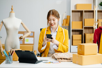 Young woman running online store Startup small business SME, using smartphone or tablet taking...