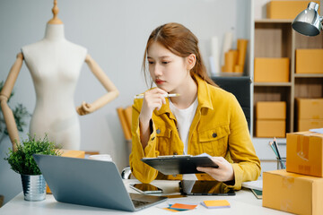 Young  woman prepare parcel box and standing check online orders for deliver to customer on tablet,...