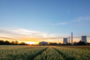 The morning in a wheat field in the background a coal-fired power station at sunrise. Landscape shot of nature and industry at the Staudinger power plant, Hainburg, Bavaria, Germany