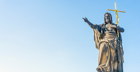 Prague, Czech Republic. Panoramic over ancient statue of Saint John of Nepomuk with cross at the Charles Bridge in Prague at blue sky sunset colors with copy space