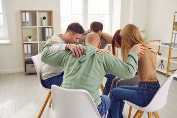 Diverse group of people is embracing in a circle during a psychotherapy session. They show support,...