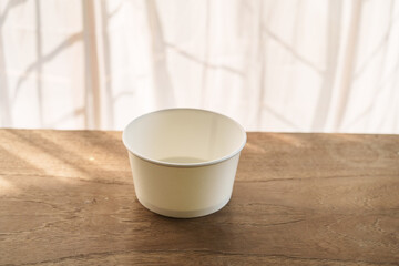 A food paper bowl rests on a brown wooden desk indoors