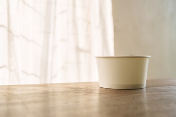 A food paper bowl rests on a brown wooden desk indoors