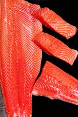 Freshly sliced salmon fillets against black backdrop emphasize vibrant color and texture of this healthy food choice, rich in omega-3 fatty acids, appealing to health-conscious consumers