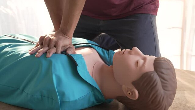 Close-up of middle-aged Asian male hands performing cardiopulmonary resuscitation (CPR) on a training dummy. Vital techniques include defibrillation, chest compressions, and maintaining the airway.