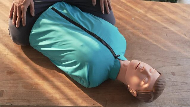 Close-up of middle-aged Asian male hands performing cardiopulmonary resuscitation (CPR) on a training dummy. Vital techniques include defibrillation, chest compressions, and maintaining the airway.
