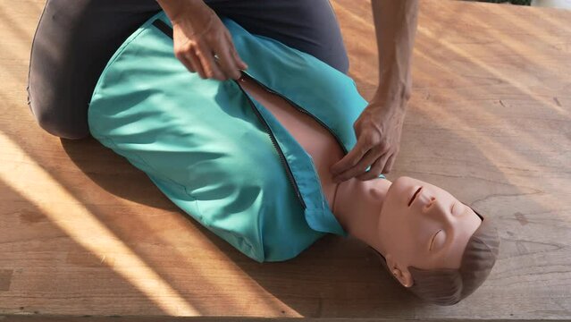 Close-up of middle-aged Asian male hands performing cardiopulmonary resuscitation (CPR) on a training dummy. Vital techniques include defibrillation, chest compressions, and maintaining the airway.