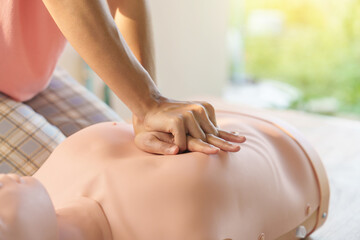 Close-up of young Asian female hands performing cardiopulmonary resuscitation (CPR) on a training...