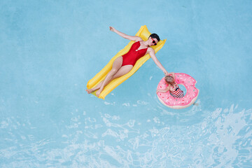 Vacation with a family. Top view of happy young mother and her daughter on the air mattreses having fun in swimming pool.