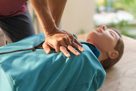 Close-up of middle-aged Asian male hands performing cardiopulmonary resuscitation (CPR) on a training dummy. Vital techniques include defibrillation, chest compressions, and maintaining the airway.