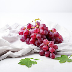 Bunch of ripe red grapes lies on a crumpled linen fabric with green leaves, isolated on a white background