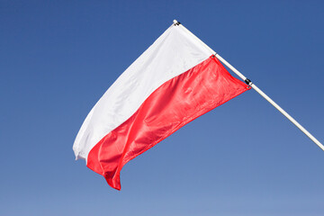 Polish flag waving on wind. Proud country symbol. National flag white and red color. Memorial place outdoor in a park. Silk fabric waves isolated on blue sky.