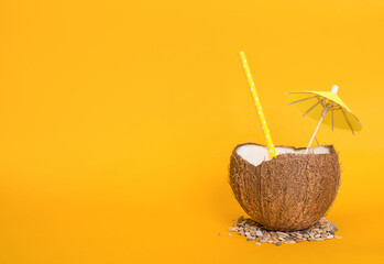 Exotic cocktail served in coco shell, drinking straw and cocktail umbrella on blorange background...