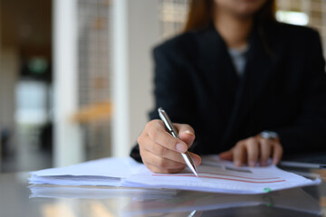 Focused on businesswoman hand writing on paper, filling paper business document at office desk