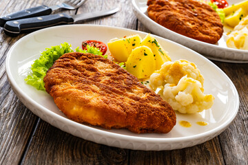 Crispy breaded fried pork chop, boiled potatoes and cooked cauliflower on wooden table
