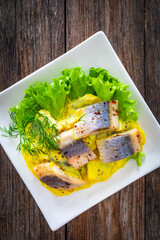 Marinated herring fillets in mustard sauce with dill and lettuce on wooden table

