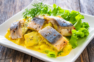 Marinated herring fillets in mustard sauce with dill and lettuce on wooden table
