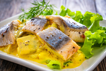 Marinated herring fillets in mustard sauce with dill and lettuce on wooden table
