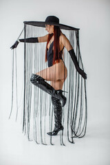 A red-haired girl in a black bodysuit, patent leather boots, gloves and a hat with threads stands...