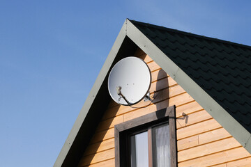 Tile roof antenna background. TV satelite dish old house roof. Countryside village architecture rooftop satelite. Television antenna mount. Orange wood house facade with mounted satellite.