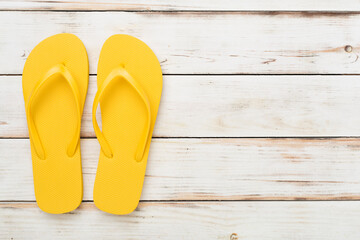 Bright yellow flip-flops on wooden background, top view. Summer concept