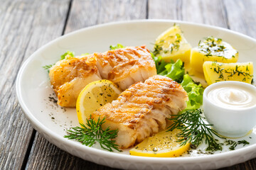 Fried codfish loin boiled potatoes and fresh vegetable salad on wooden table