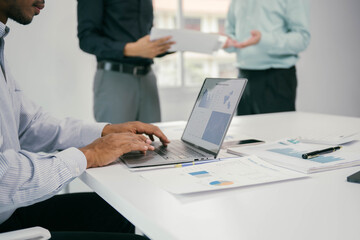 Fototapeta premium A man is typing on a laptop in front of a table with papers and a cell phone