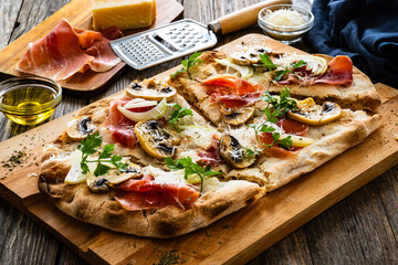 Roman Pinsa with mozzarella cheese, ripening ham and mushrooms on wooden table