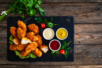 Fried breaded chicken nuggets served with mayonnaise, ketchup and mustard on wooden table
