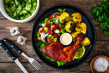 Oven roasted chicken thigh with boiled potatoes and fresh vegetables on wooden table
