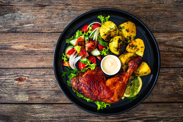 Oven roasted chicken thigh with boiled potatoes and fresh vegetables on wooden table
