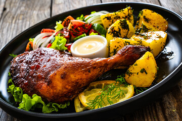 Oven roasted chicken thigh with boiled potatoes and fresh vegetables on wooden table
