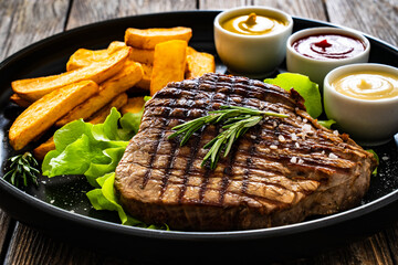 Grilled beef sirloin steak with French fries on wooden table
