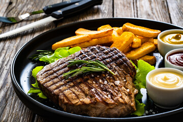 Grilled beef sirloin steak with French fries on wooden table
