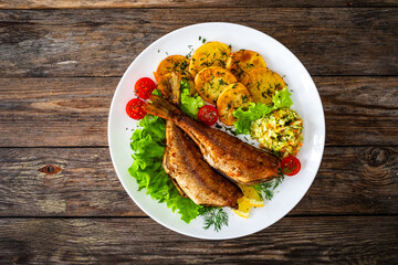 Fried sea bass with fried potatoes and fresh cabbage salad on wooden table

