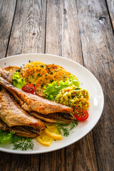 Fried sea bass with fried potatoes and fresh cabbage salad on wooden table

