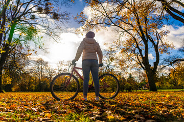 Woman riding bicycle in city forest in autumnal scenery
