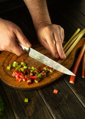 Chef hands using a knife to cut rheum plant on a kitchen board before preparing vitamin salad for...