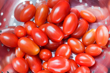 Roma tomatoes background. Washing vegetables before eating. Shiny metal colander to drain water while washing. Healthy salad preparation.