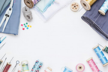 Elegant photo of fabric, sewing tools, sewing accessories, sewing threads, thread spools, needles, pins on the white table with copy space