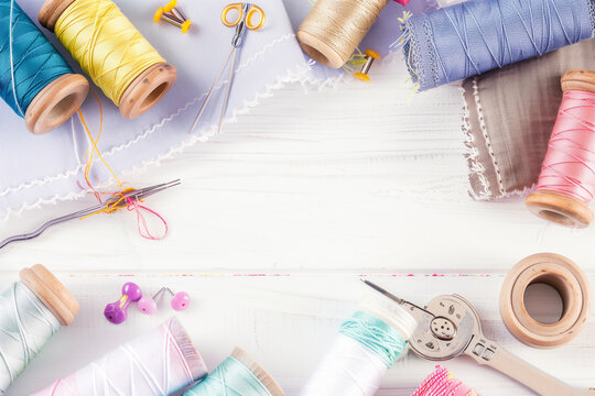  Flat elegant photo of different fabric and sewing tools, sewing accessories, sewing threads, thread spools, needles, pins on the white table with copy space
