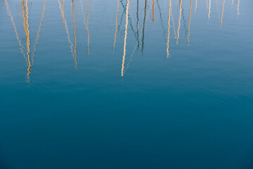 Summer image of sailing boats colorful masts reflected on sea water. Abstract summer blue nautical background.